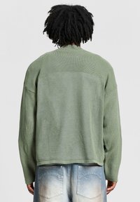 Losse, olijfgroene trui van gebreide stof met textuur, met verlaagde schouders en een ronde halslijn. Zichtbare naaien aan de achterkant.