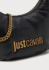Sac à main en cuir noir avec une chaîne dorée et un logo "justcavalli" embossé. Présente une texture lisse et une forme croissante structurée.