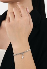 Silberne Kettenarmband mit einem kleinen Handanhänger, gestaltet mit ineinander greifenden Gliedern und einem polierten Finish. Die Textur wirkt glatt und glänzend.