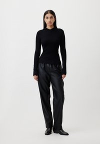 Čierny rebrovaný pletený top s kapucňou skombinovaný s čiernymi nohavicami z imitácie kože a elegantnými čiernymi boots, na neutrálnom pozadí.