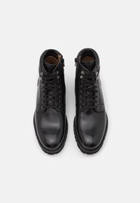 Bottes en cuir noir avec une finition lisse, présentant un design à lacets, hauteur cheville, col rembourré et zips sur les côtés pour un enfilage facile.