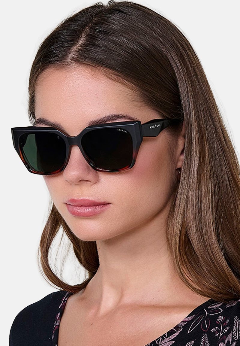 Gafas de sol de gran tamaño en negro y carey con montura angular y lentes oscuros. Presentan un sutil logotipo en las patillas.