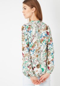 Blusa floral de tejido ligero, con flores multicolores sobre un fondo blanco, mangas largas y puños fruncidos.