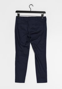 Pantaloni blu navy con vestibilità slim, realizzati in un tessuto morbido. Presentano due tasche posteriori e una parte anteriore piatta. Appesi a un gancio nero.