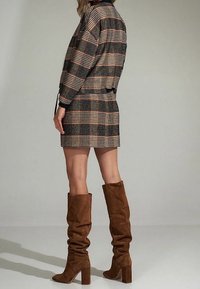 Abito blazer a quadri marrone con maniche lunghe, vita aderente e tessuto texturizzato. Stivali marroni morbidi al ginocchio con tacco a blocco.