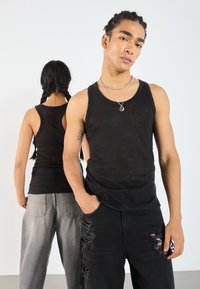 Sorte ermeløse topplater på to modeller; en med bakgrunnsvisning. Bemerkelsesverdige funksjoner inkluderer et lett stoff, slitte svarte jeans og lagdelte halskjeder.