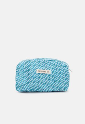 Trousse de maquillage bleue avec un motif en losanges texturé, fermeture éclair et une petite étiquette portant la mention "SUMMERY" à l'avant. Matériau en tissu doux.