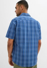 Camicia a maniche corte a quadri blu con motivo a scacchi e dettagli bianchi, colletto classico e orlo dritto sul retro.