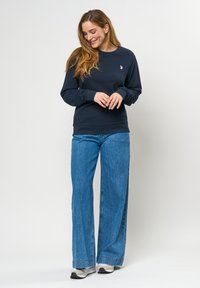 Námořnická mikina s kulatým výstřihem, žebrovanými manžetami a lemem, v kombinaci s širokými modrými džíny. Obsahuje malé vyšívané logo na hrudi.