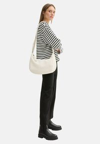 Borsa a spalla bianca con una texture liscia, indossata da un modello con una camicia a righe bianco e nera e pantaloni neri, in abbinamento a stivali neri massicci.