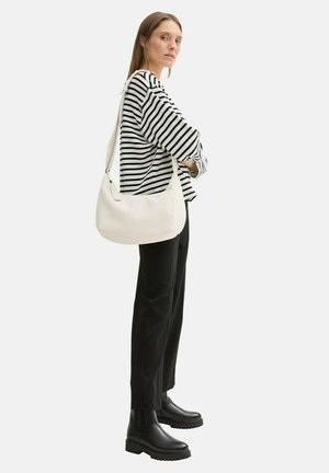Weiße Schultertasche mit einer glatten Textur, getragen von einem Model in einem schwarz-weißen gestreiften Hemd und schwarzen Hosen, ergänzt mit klobigen schwarzen Stiefeln.