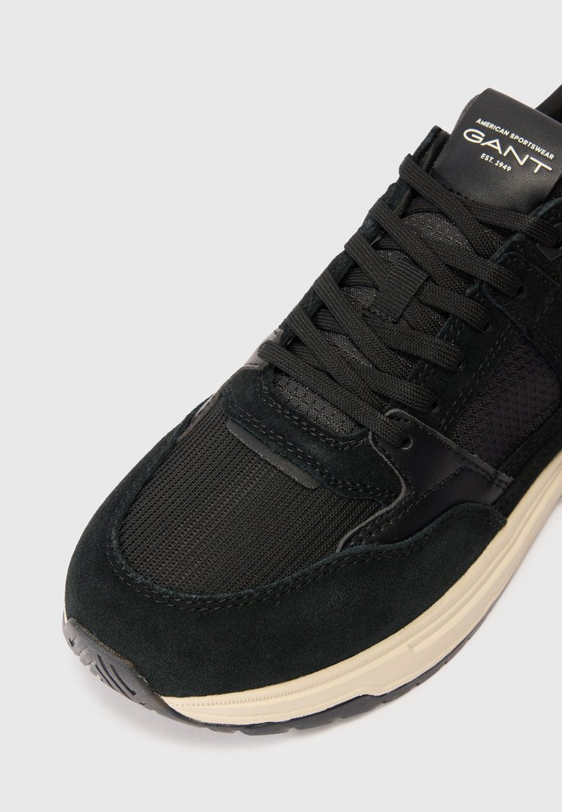 Czarne sportowe sneakersy z mieszanką zamszu i siateczki, zakrzywiony kształt, teksturowana powierzchnia oraz kremowa podeszwa średnia.