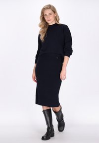 Marineblaue gerippte Strickpullover-und-Rock-Kombination, mit Rundhalsausschnitt, fallenden Schultern und knielangen schwarzen Lederstiefeln mit Schnallelementen.