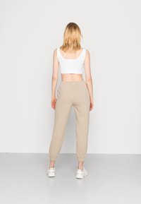 Beżowe spodnie dresowe z elastycznymi mankietami i pasem, w połączeniu z białym krótki topem na ramionach. Miękka tkanina z luźnym krojem.