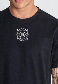 Svart bomulls t-shirt med rund halsringning, med en vit broderad logotypdesign på bröstet. Korta ärmar och slät struktur.