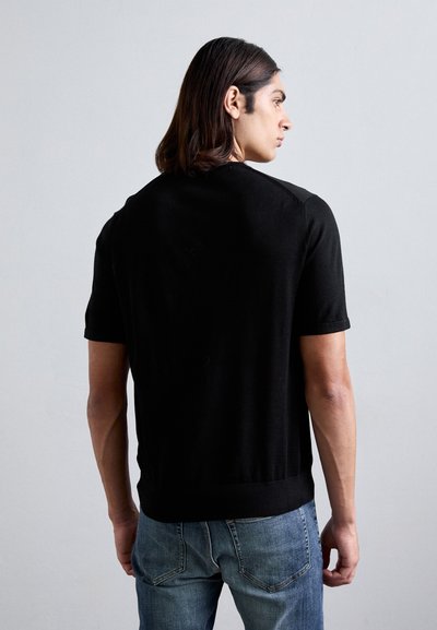 Schwarzer kurzärmeliger Strickpullover mit Rundhalsausschnitt, geripptem Saum und glatter Textur, kombiniert mit hellblauen Jeans.
