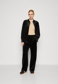 Svart fløyel loungewear-sett med knapp-up skjorte med krage og bukser med elastisk midje. Glatt tekstur med avslappet passform.
