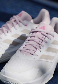 Hvide og pink Adidas atletiksko med snørebånd, tre beige striber på siden og Adidas-logo på tungen.
