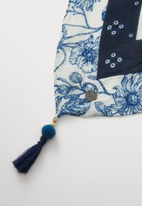 Šal s cvjetnim uzorkom u svijetloj krem i plavoj boji, s mornarsko plavim akcentom i detaljem od rese i pom-poma u jednom kutu.