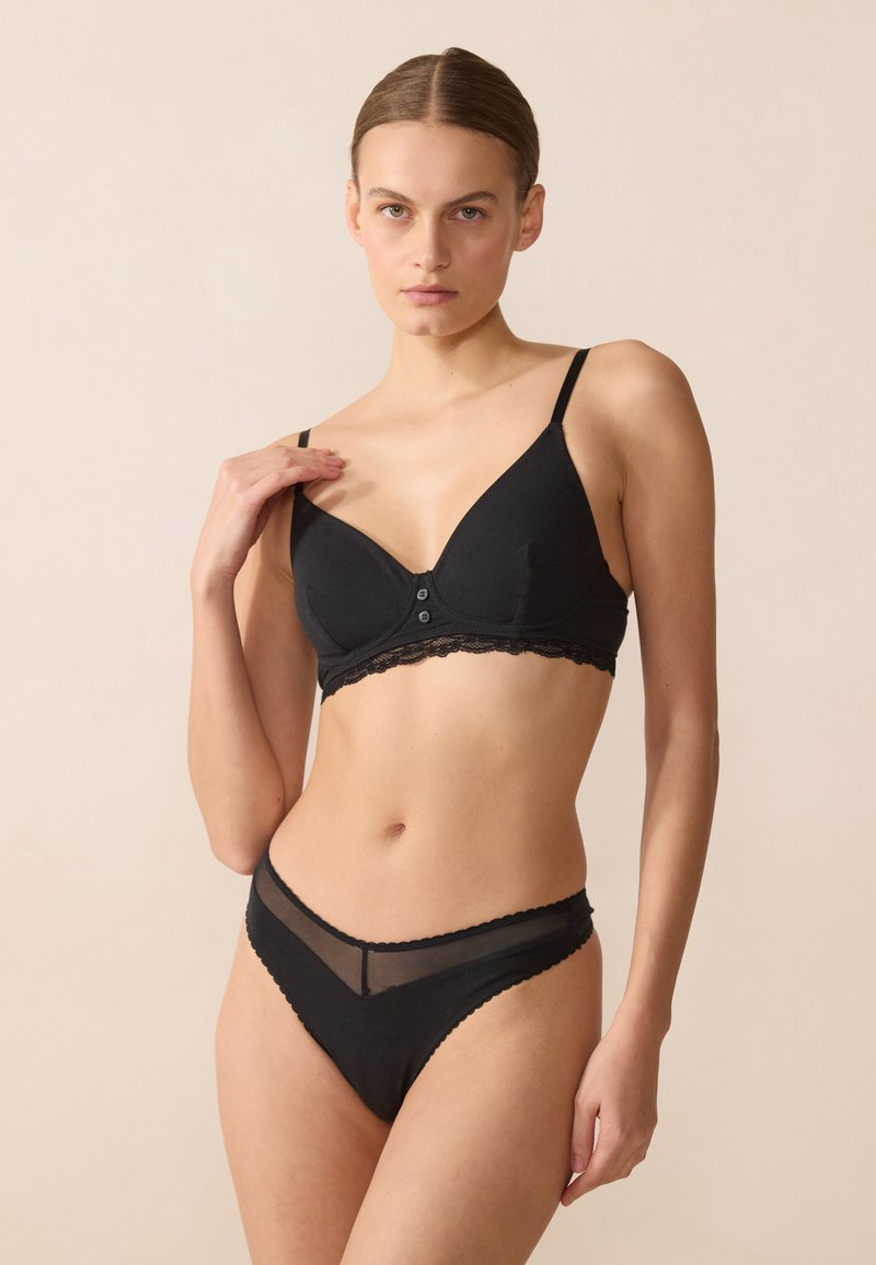 Zwart beha- en broekje-set van gladde stof. De beha heeft kantdetails en een knoopsluiting; het broekje heeft doorschijnende accenten en geschulpte randen.