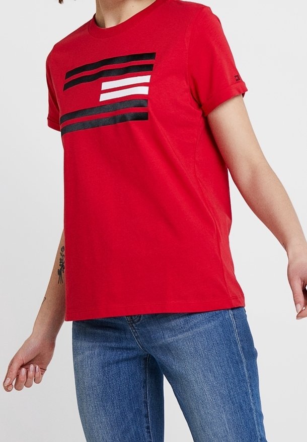 Mujer vestida con una camiseta roja con rayas horizontales en blanco y negro, combinada con jeans azules, mostrando un estilo casual.