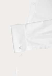 Biały mankiet koszuli z srebrnym spinkiem w kształcie węzła, widoczne guziki wzdłuż pliski rękawa na jednolitym białym tle.