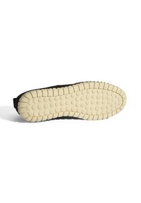 Semelle de sneaker noire avec une surface texturée, dotée d'une semelle extérieure en caoutchouc crème et d'un motif de traction circulaire, conçue pour l'adhérence.
