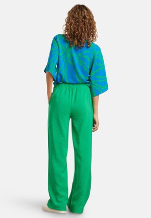 Overmaatse blauwe shirt met groen abstract patroon, gecombineerd met losse, gestructureerde groene broek. Ontspannen pasvorm, rechte pijpen, casual stijl.