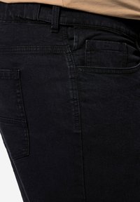 Jeans de mezclilla negra con una textura suave, que cuentan con un bolsillo lateral y una cintura en posición sentada. Diseño simple sin acentos de hardware visibles.