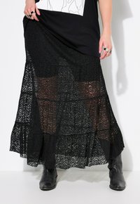 Schwarzer Spitzen-Maxi-Rock mit gestuftem Design, durchscheinendem Überwurf, kompliziertem Muster und Rüsche am Saum, kombiniert mit schwarzen Stiefeletten.