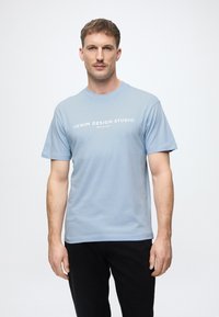 Ανοιχτό μπλε κοντομάνικο μπλουζάκι από βαμβάκι, με λευκό λογότυπο "DENIM DESIGN STUDIO" εκτυπωμένο μπροστά. Μαλακή υφή, κλασική εφαρμογή.