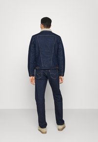 Tmavě modrá džínová bunda s šedým beránkovým límcem, vyznačující se přiléhavým střihem a zadními švy. Doplněno o kvalitní tmavě modré džínové kalhoty.