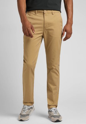 Beige Chinos mit geradem Bein, gefertigt aus glattem Stoff, mit Knopfverschluss, Gürtelschlaufen und Fronttaschen. Kombiniert mit grauen Sneakers.