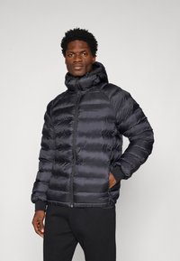 Giacca a vento nera con zip frontale, dotata di cappuccio, design trapuntato e dettagli con polsini elasticizzati. Texture liscia e lucida.