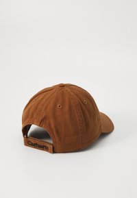 Brown cotton cap with a curved brim, featuring a textured fabric, six-panel design, and a Carhartt logo on the adjustable strap.