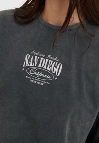 Dark gray cotton t-shirt featuring a vintage-style white print with "SAN DIEGO, California" and decorative elements. Crew neck design.