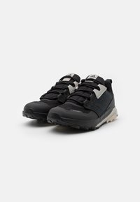 Zapatillas deportivas negras con parte superior de malla texturizada, acentos grises, puntera reforzada y suela resistente. Presenta cordones elásticos y logotipo en la lengüeta.