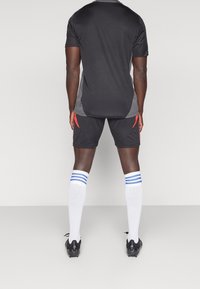 Maglia sportiva nera con dettagli grigi, abbinata a pantaloncini neri con decorazioni rosse. Calze bianche lunghe fino al ginocchio con strisce blu, scarpe da calcio nere.