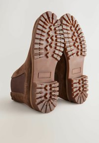 Brown suede ankle boots with a textured rubber sole featuring deep grooves and an ankle height. Side elastic panels for easy wearing.