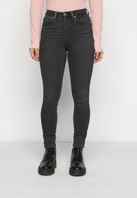 Jeans skinny negros de tiro alto con una textura suave, diseño de cinco bolsillos y cierre frontal de botón, combinados con botas negras de cordones.
