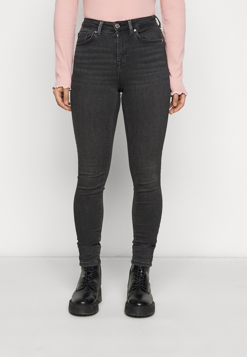 Jeans skinny negros de tiro alto con una textura suave, diseño de cinco bolsillos y cierre frontal de botón, combinados con botas negras de cordones.