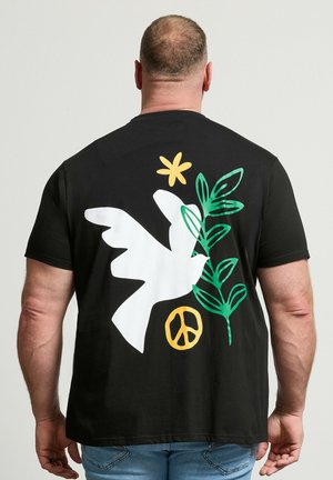Mann trägt schwarzes T-Shirt mit weißer Taube, grünem Zweig, gelber Blume und gelbem Friedenssymbol auf dem Rücken bedruckt.