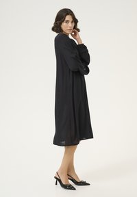 Svart långärmad klänning i lätt tyg, med en l�ös passform och subtil textur. Tillsammans med svarta slingbacks med spetsig tå.