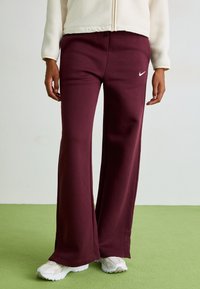 Mörkröda sweatpants gjorda av mjukt tyg, med en avslappnad passform, subtila sidoslitsar och en liten vit Nike-logotyp på vänster lår.
