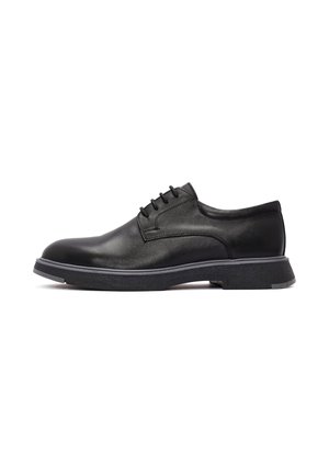 Chaussure oxford en cuir noir avec un bout arrondi, un design à lacets et une semelle en caoutchouc texturée. Présente un accent gris subtil sur le bord de la semelle.