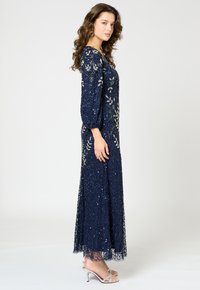 Mörkblå klänning med långa puffärmar, dekorerad med silverblommönster och paljetter. Transparent nederdel med detaljerad textur; matchas med silverfärgade klackar.