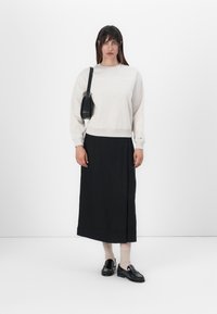 Lichtgrijze sweatshirt met logo aan de voorkant, gecombineerd met een zwarte midi-jurk. Zwarte instappers en een kleine zwarte handtas maken de look compleet.