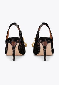 Des escarpins slingback en velours noir avec un talon aiguille fin, des accents en matériel doré et des motifs texturés élaborés sur la tige.
