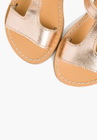 Sandali metallici rosa oro con design a T, tomaia in pelle liscia e suola in pelle marrone chiaro con cuciture a contrasto.