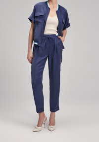 Granatowa kurtka zapinana na zamek, z krótkimi rękawami i dwiema przednimi kieszeniami; zestawiona ze spodniami w tym samym kolorze, które mają elastyczny pas i podwinięte nogawki.